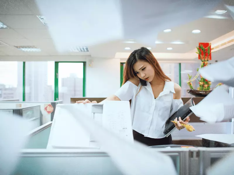 Busy woman using a photocopier and talking on a cellphone.
